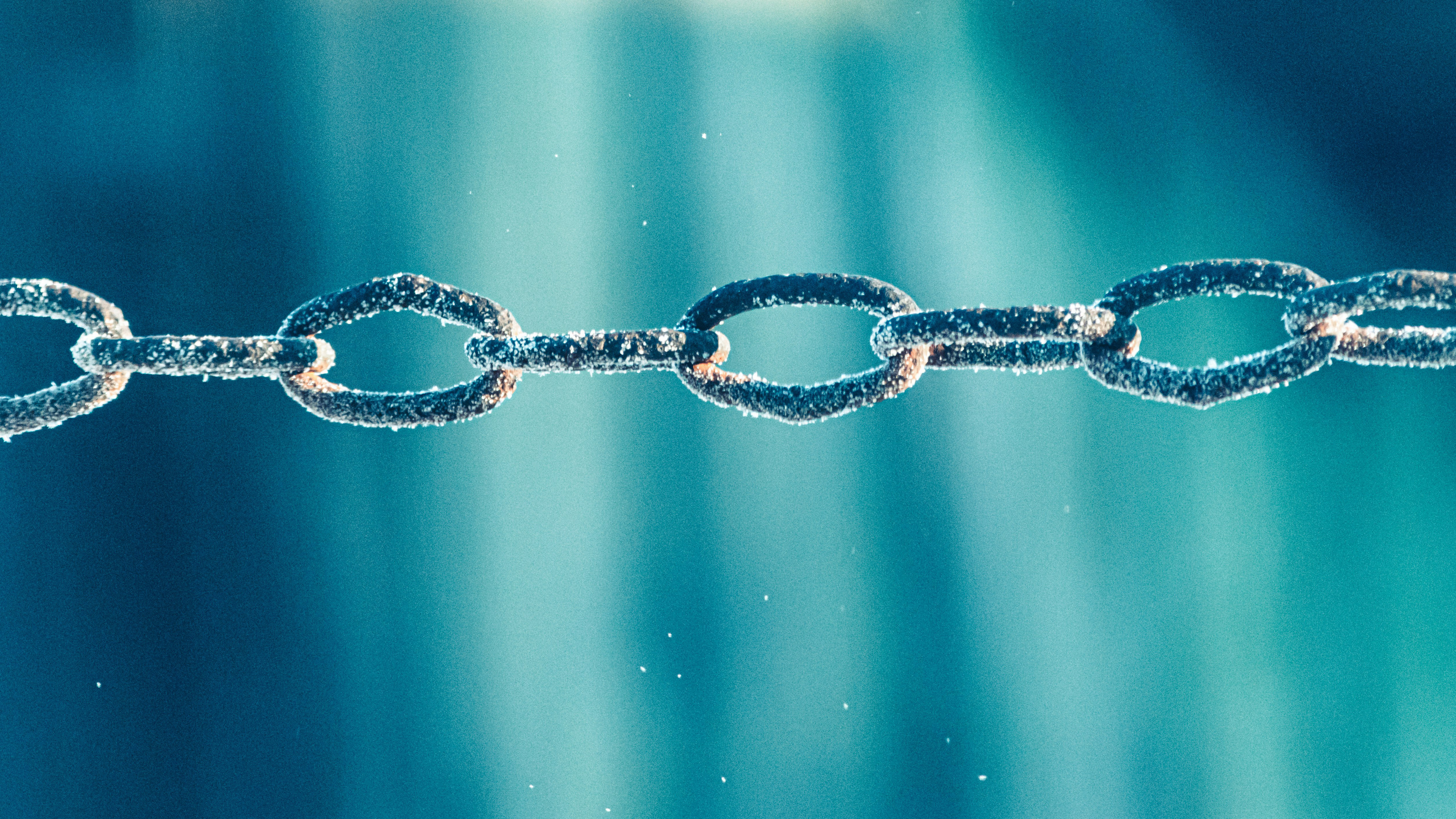 Close-up of a frost-covered metal chain against a blue background.
